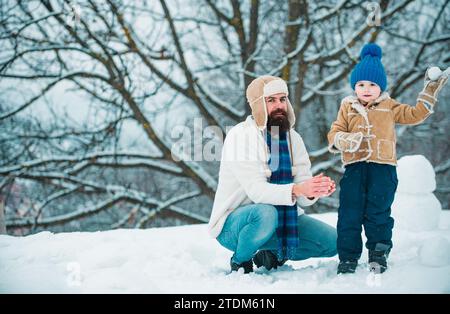 Heureux père et fils jouent sur Noël d'hiver. Fête des pères. Enfant heureux jouant avec boule de neige sur fond blanc d'hiver. Heureux amour Banque D'Images