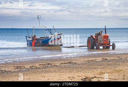 tracteurs tirant des bateaux de pêche de la mer sur la plage à marske par la mer dans le nord du yorkshire Banque D'Images