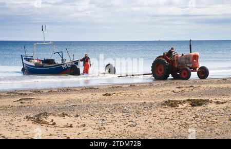 tracteurs tirant des bateaux de pêche de la mer sur la plage à marske par la mer dans le nord du yorkshire Banque D'Images