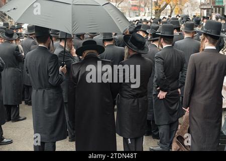 Des hommes juifs orthodoxes vêtus de noir assistent aux funérailles d'un rabbin hassidique et écoutent un éloge. À Brooklyn, New York. Banque D'Images