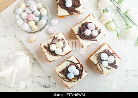 Barres de gâteau aux carottes de Pâques décorées avec nid de chocolat et œufs de bonbons au chocolat fleurissant des fleurs de cerise ou de pomme sur des fonds rustiques en bois clair. Banque D'Images