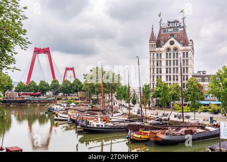 Le vieux port de Rotterdam avec des bateaux fluviaux, surplombé par le bâtiment historique Witte huis et les pylônes rouges du Willemsbrug, sous un ciel orageux. Banque D'Images