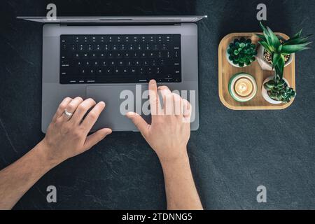 Vue de dessus, un homme utilise un ordinateur portable et des pots de fleurs sur un fond sombre. Banque D'Images