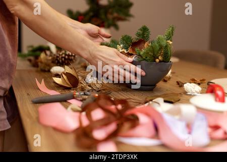 Mains féminines créant un décor artisanal de Noël avec des branches de sapin. Banque D'Images