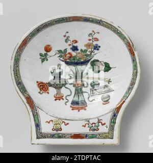 Bol en forme de coquille Saint-Jacques avec antiquités, anonyme, c. 1700 - c. 1724 bol en forme de coquille en porcelaine avec paroi nervurée, peint sur le glaçage en bleu, rouge, vert, jaune, aubergine, noir et or. Sur le sol des antiquités (vase à fleurs, ruyi-skept, brûleur d'encens etc.) ; sur la poignée deux symboles chanceux (parasol, pêche) ; Lotus boissons stylisées sur le bord contre un sol vert moucheté noir. Dos du dos. Famle verte. Porcelaine de Chine. glaçage. cobalt (minéral). Or (métal) peinture / dorure / vitrification bol en forme de coquille de porcelaine avec paroi nervurée, peint sur la glaçure en bleu, rouge, gre Banque D'Images