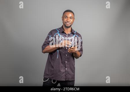 Joyeux homme noir millénaire dans Casual en utilisant un téléphone intelligent moderne, en vérifiant les médias sociaux, en regardant l'espace de copie pour l'application mobile Banque D'Images