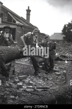 Années 1950, historique, trois travailleurs masculins défrichant une vieille unité industrielle, debout près d'un arbre tombé pour une photo, avec une scie manuelle assise dans le tronc de l'arbre, Angleterre, Royaume-Uni. Banque D'Images