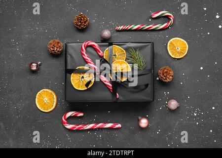 Boîte cadeau de Noël avec des tranches d'orange séchées, des cannes de bonbons et des pommes de pin sur fond noir Banque D'Images