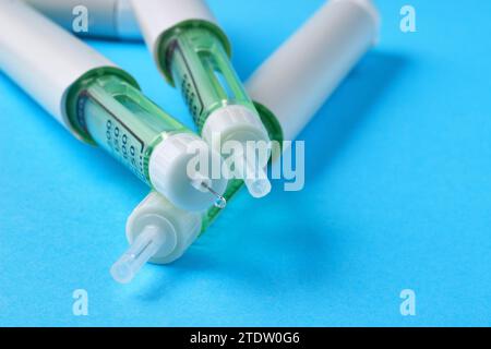 Stylo de seringue d'insuline avec une goutte de médicament à l'extrémité de l'aiguille sur un fond bleu Banque D'Images