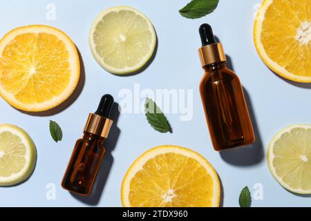Bouteilles de sérum cosmétique, agrumes tranchés et feuilles vertes sur fond bleu clair, pose plate Banque D'Images