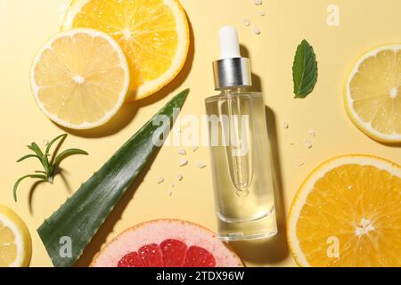 Bouteille de sérum cosmétique, agrumes tranchés et feuille d'aloe vera sur fond jaune, mise à plat Banque D'Images