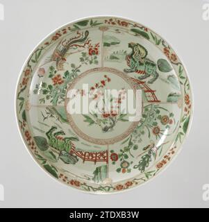 Soucoupe-plat avec glaçure de céladon, sprays prunus, shishi, paon et huangs feng, anonyme, c. 1700 - c. 1724 soucoupe en porcelaine avec un mur rond, recouverte d'une glaçure verte, peinte en bleu glacé sous-jacent et sur la glaçure rouge, vert, jaune, aubergine, noir et or. Le plat est, sauf à l'intérieur de l'anneau de pied, recouvert d'un émail celadongroen. Sur le plat un médaillon avec une branche de prunus ; autour de quatre compartiments, deux avec shishi (chien lion), un avec Feng Huang et un avec un paon ; le bord avec des branches de prunus ; le dos avec trois branches de fleurs ; Un double cercle sur le fond. Suspension sy Banque D'Images