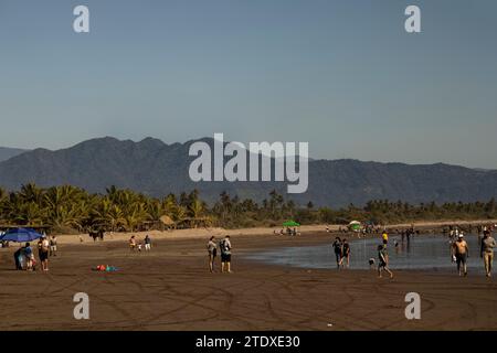 Un mélange captivant de soleil, de sable et de mer, où les amateurs de plage rencontrent l'horizon, encadrés par des montagnes lointaines dans l'étreinte d'une évasion côtière. Banque D'Images