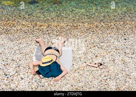 Torri del Benaco : Femme couchée face cachée sur la plage, chapeau de soleil, bikini, Lago di Garda (Lac de Garde) à Vérone, Vénétie, Italie Banque D'Images