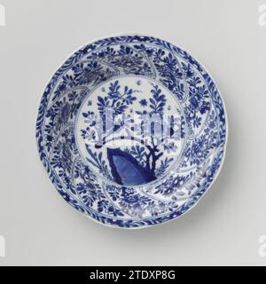 Soucoupe avec panneaux torsadés et sprays de fleurs, anonyme, c. 1680 - c. 1720 soucoupe en porcelaine avec mur rond modelé en dix cours torsadés, peinte en bleu sous-couche. Sur le plat un rocher avec une branche de fleur, des plantes et un papillon ; Une branche de fleur sur le mur dans chaque boîte ; le bord avec une boisson de fleur ; sur le dos aussi une branche de fleur dans chaque boîte. Marqué sur la face inférieure du caractère chinois « Fú » dans un double cercle. Bleu blanc. Porcelaine de Chine. glaçage. Cobalt (minéral) peinture / vitrification soucoupe en porcelaine avec paroi ronde modelée en dix parcours torsadés, peinte en bleu sous-couche. Sur le Banque D'Images