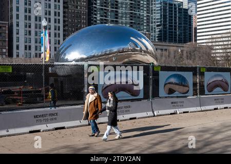 Chicago, États-Unis. 19 décembre 2023. Les touristes passent une clôture entourant la zone autour de l'installation artistique appelée Cloud Gate dans Millennium Park par l'artiste britannique Anish Kapoor. Populairement connue sous son surnom The Bean, l’installation artistique est l’une des principales attractions touristiques de Chicago. Les travaux de réparation se poursuivront jusqu'au printemps 2024 avec des améliorations au pavage et d'autres réparations. Crédit : Stephen Chung / Alamy Live News Banque D'Images