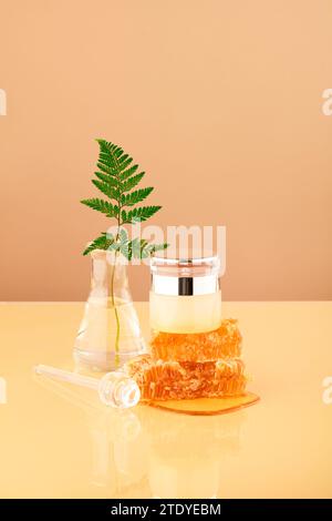 Une feuille de fougère est insérée dans un flacon erlenmeyer, un pot cosmétique luxueux placé sur de la cire d'abeille brute naturelle. Le miel a la capacité de stimuler le collagène Banque D'Images