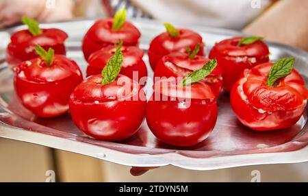 Une vue sur une cuisine rustique avec un plateau en métal contenant de délicieuses tomates farcies maison décorées avec des feuilles de menthe fraîche Banque D'Images