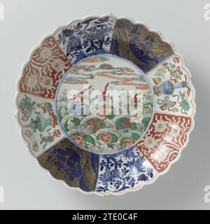 Soucoupe-plat avec côtés cannelés et fleurs et crustacés au-dessus des vagues, anonyme, c. 1700 - c. 1724 bol en porcelaine avec paroi nervurée et bord lobé, peint en bleu sous glaçure et sur le glaçage bleu, rouge, vert, jaune, aubergine, noir et or. Sur le plat un médaillon avec des fleurs de prunus et des crustacés au-dessus des vagues tourbillonnantes ; le mur divisé en huit compartiments avec la même décoration de l'autre côté: des vignes de Lotus sauvées contre un sol rouge, des arbres fleuris avec oiseau et papillon, un paysage en or contre un bleu pouddré (poudre -bleu) sol et symboles de bonheur (trépied, vase avec paon s Banque D'Images