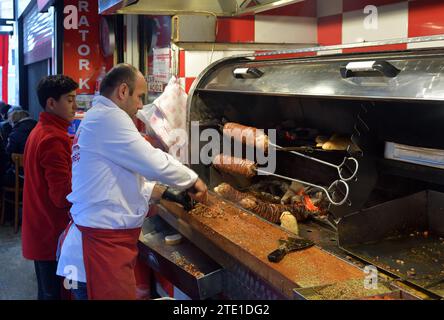 Istanbul, Turquie - 08 décembre 2023 : un turc, chef cuisinier de kokorecci coupant une brochette de viande pour un Kokorec, ou sandwich kokoretsi Banque D'Images