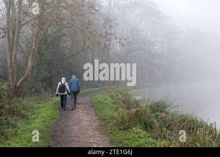 Un très vieux couple marchant le long du canal de navigation River Wey un jour d'hiver très brumeux Weybridge Surrey Angleterre Royaume-Uni Banque D'Images