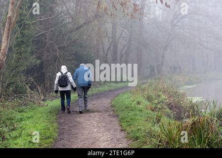 Un très vieux couple marchant le long du canal de navigation River Wey un jour d'hiver très brumeux Weybridge Surrey Angleterre Royaume-Uni Banque D'Images