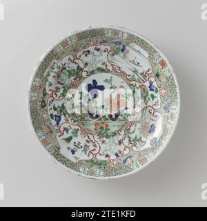 Soucoupe-plat avec des animaux (mythologiques), paysage et sprays de fleurs, anonyme, c. 1700 - c. 1724 soucoupe en porcelaine avec mur rond, peinte en bleu glacé et sur le glaçage bleu, rouge, vert, jaune, aubergine, noir et or. Sur le plat un médaillon avec deux oiseaux et des branches de fleurs ; autour du médaillon quatre cours avec un Feng Huang, un paysage avec une figure dans un bateau, un Qilin et des symboles chanceux, quatre cours plus petits avec des plantes à fleurs; entre les cours des zones florales et des papillons contre un sol vert moucheté noir ; le bord avec des vignes de fleurs stylisées dans un cartouche intercalaires Banque D'Images