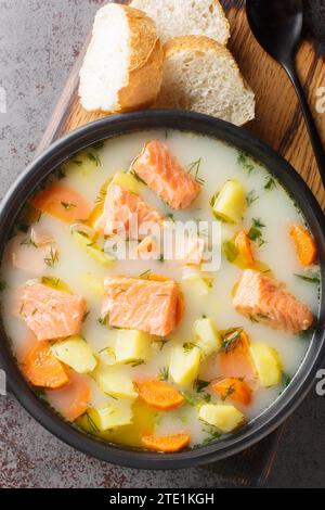 Soupe finlandaise de saumon sauvage avec crème et légumes-racines gros plan sur une assiette sur la table. Vue verticale de dessus Banque D'Images