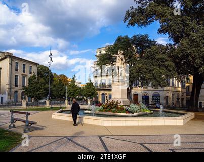 Nîmes, France - 4 octobre 2023 : un vieil homme passe devant une ancienne fontaine romaine avec la statue d'Antonin à Nîmes. Banque D'Images