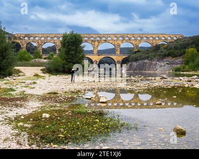 Pont du Gard, France - 4 octobre 2023 : Femme séjournant sous le célèbre pont romain du Gard, qui se reflète dans la rivière Gardon Banque D'Images