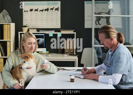 Propriétaire de chien femelle parlant à un vétérinaire masculin pendant qu'il écrit une ordonnance médicale pour son animal de compagnie Banque D'Images
