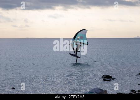 Un foil surfer sur la mer calme à pleine vitesse. Avec une voile verte et quelques rochers dans l'eau au premier plan Banque D'Images