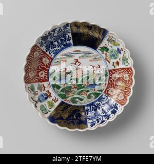 Soucoupe-plat avec côtés cannelés et fleurs et crustacés au-dessus des vagues, anonyme, c. 1700 - c. 1724 bol en porcelaine avec paroi nervurée et bord lobé, peint en bleu sous glaçure et sur le glaçage bleu, rouge, vert, jaune, aubergine, noir et or. Sur le plat un médaillon avec des fleurs de prunus et des crustacés au-dessus des vagues tourbillonnantes ; le mur divisé en huit cours avec la même décoration de l'autre côté: Lotus vrilanks sauvé contre un sol rouge, arbres fleuris avec oiseau et papillon, un paysage en or contre un bleu poudré (bleu poudré) sol et coûteux (Artemisiablad) avec des symboles chanceux (trois - Banque D'Images