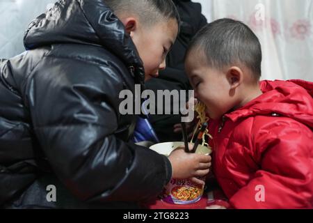 (231220) -- LINXIA, 20 déc. 2023 (Xinhua) -- des enfants ont des nouilles instantanées à l'intérieur d'une tente sur un site de relocalisation temporaire dans le village de Taojia, dans le comté de Jishan, dans la province du Gansu, au nord-ouest de la Chine, 20 déc. 2023. Des opérations de sauvetage et de secours sont en cours dans un climat de froid intense alors qu'un tremblement de terre de magnitude 6,2 a tué 113 personnes et blessé 782 autres dans la province du Gansu, dans le nord-ouest de la Chine, selon une conférence de presse donnée mercredi. Au total, 87 076 personnes de 20 457 ménages ont été temporairement réinstallées dans des lieux sûrs. Matériel de secours d'urgence tels que tentes, couettes, lits pliants et mois Banque D'Images