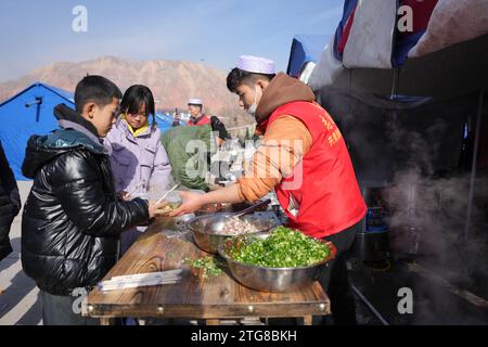 (231220) -- LINXIA, 20 déc. 2023 (Xinhua) -- Un membre du personnel de l'entreprise distribue gratuitement des nouilles de bœuf sur un site de relocalisation temporaire dans le village de Dahe, dans le comté de Jishan, dans la province du Gansu, au nord-ouest de la Chine, le 20 décembre 2023. Des opérations de sauvetage et de secours sont en cours dans un climat de froid intense alors qu'un tremblement de terre de magnitude 6,2 a tué 113 personnes et blessé 782 autres dans la province du Gansu, dans le nord-ouest de la Chine, selon une conférence de presse donnée mercredi. Au total, 87 076 personnes de 20 457 ménages ont été temporairement réinstallées dans des lieux sûrs. Matériel de secours d'urgence tels que tentes, courtepointes, foldi Banque D'Images