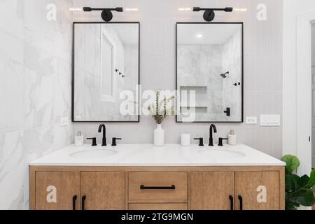 Une salle de bains avec des carreaux de métro verticaux en marbre et empilés, un meuble-lavabo en chêne blanc, des miroirs carrés encadrés de noir et des robinets, et un comptoir en marbre. Banque D'Images