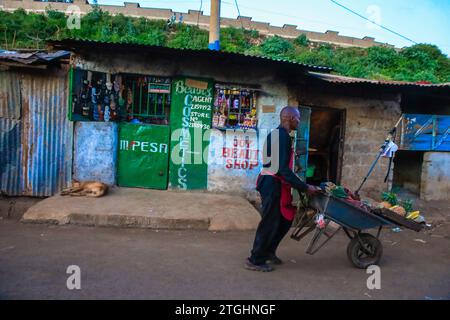 NAIROBI, Afrique. 19 décembre 2023. Un homme passe devant les rues vendant des fruits sur sa brouette dans le bidonville de Kibera, Nairobi. Une vue à travers la vie quotidienne à Kibera actuellement le plus grand bidonville d'Afrique et les activités commerciales quotidiennes effectuées par les résidents locaux. (Image de crédit : © Donwilson Odhiambo/ZUMA Press Wire) USAGE ÉDITORIAL SEULEMENT! Non destiné à UN USAGE commercial ! Banque D'Images