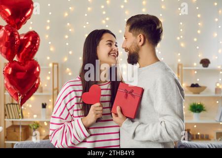 Heureux couple souriant dans l'amour dans l'atmosphère romantique dans les bras de l'autre, tenant le coeur rouge et la boîte cadeau Banque D'Images