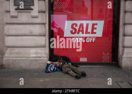 Un homme sans abri se trouve dans la rue devant un panneau DE VENTE 70% de réduction sur Piccadilly Circus de Londres, pendant la période de Noël, Angleterre, Royaume-Uni Banque D'Images