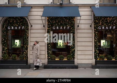 Une femme s'arrête pour bailler en prenant un appel sur son smartphone le long de Old Bond Street au cœur de Mayfair à Londres, le 20 décembre 2023. Banque D'Images