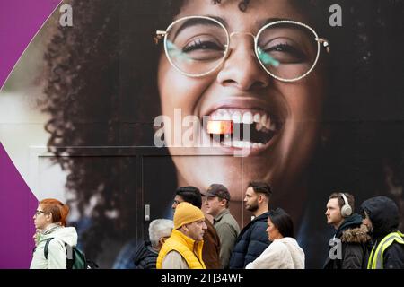 Des acheteurs de Noël et un panneau d'affichage pour un nouveau point de vente d'opticien pour Vision Express sur Oxford Street, le 20 décembre 2023, à Londres, Angleterre. Banque D'Images