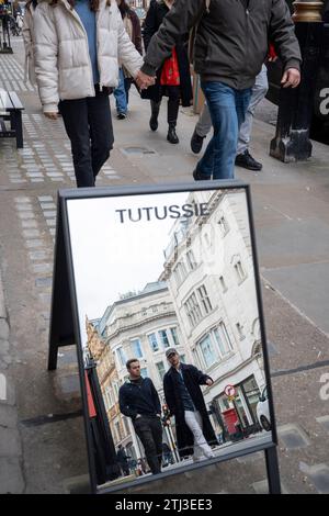 Les acheteurs de Noël dans un miroir de rue devant le détaillant Tutussie à Mayfair, le 20 décembre 2023, à Londres, Angleterre. Tutussie a commencé à l'origine comme une marque de vêtements d'extérieur en cachemire, s'étendant dans d'autres catégories, tout en gardant toujours la slow fashion et la durabilité. Banque D'Images