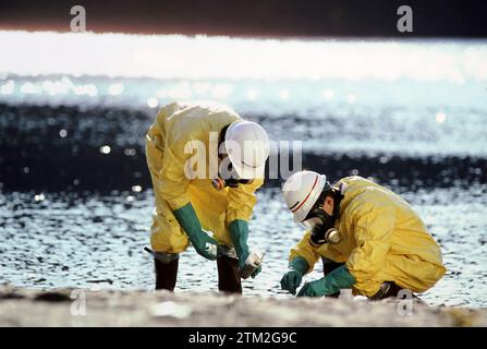 Deux techniciens portant des vêtements de protection examinant des déchets toxiques trouvés sur une rive Banque D'Images