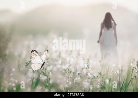 un papillon blanc vole librement au milieu d’un pré fleuri tandis qu’une femme marche en arrière-plan, concept abstrait Banque D'Images