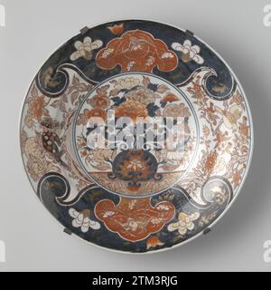 Plat avec un vase à fleurs, huangs feng, shishi et oiseaux, anonyme, c. 1700 - c. 1750 soucoupe en porcelaine, peinte en bleu glacé et sur le glaçage rouge, noir et or. Sur le plat un double médaillon avec un vase à fleurs avec des chrysanthèmes et des pivoines. Le mur et le bord sont divisés en quatre compartiments avec deux shishi (chien lion) dans un paysage, deux oiseaux sur une branche d'un arbre de prunus et deux fois un cartouche en forme de Ruyi avec un Fenghuang sur un fond bleu avec des vignes fleuries. Le plat est pris dans un cadre métallique. Probablement un européen (français ?) Imitation de l'Imari japonais. Europe Porcelai Banque D'Images