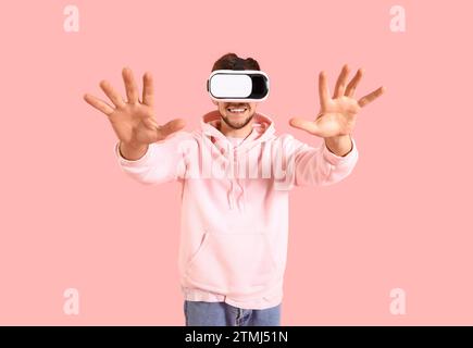 Jeune homme barbu utilisant des lunettes VR sur fond rose Banque D'Images