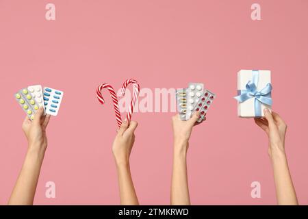 Mains féminines tenant des pilules dans des blisters, boîte-cadeau et canne à sucre sur fond rose Banque D'Images