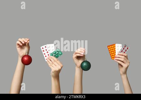 Mains féminines tenant des pilules dans des blisters et des boules de Noël sur fond gris Banque D'Images