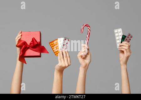 Mains féminines tenant des pilules dans des blisters, canne à sucre et boîte-cadeau sur fond gris Banque D'Images