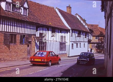 Une scène de steet de Lavennam Suffolk Angleterre, capturée en 1986, l'image montre deux voitures de l'époque sur une rue de Lavenham. Banque D'Images